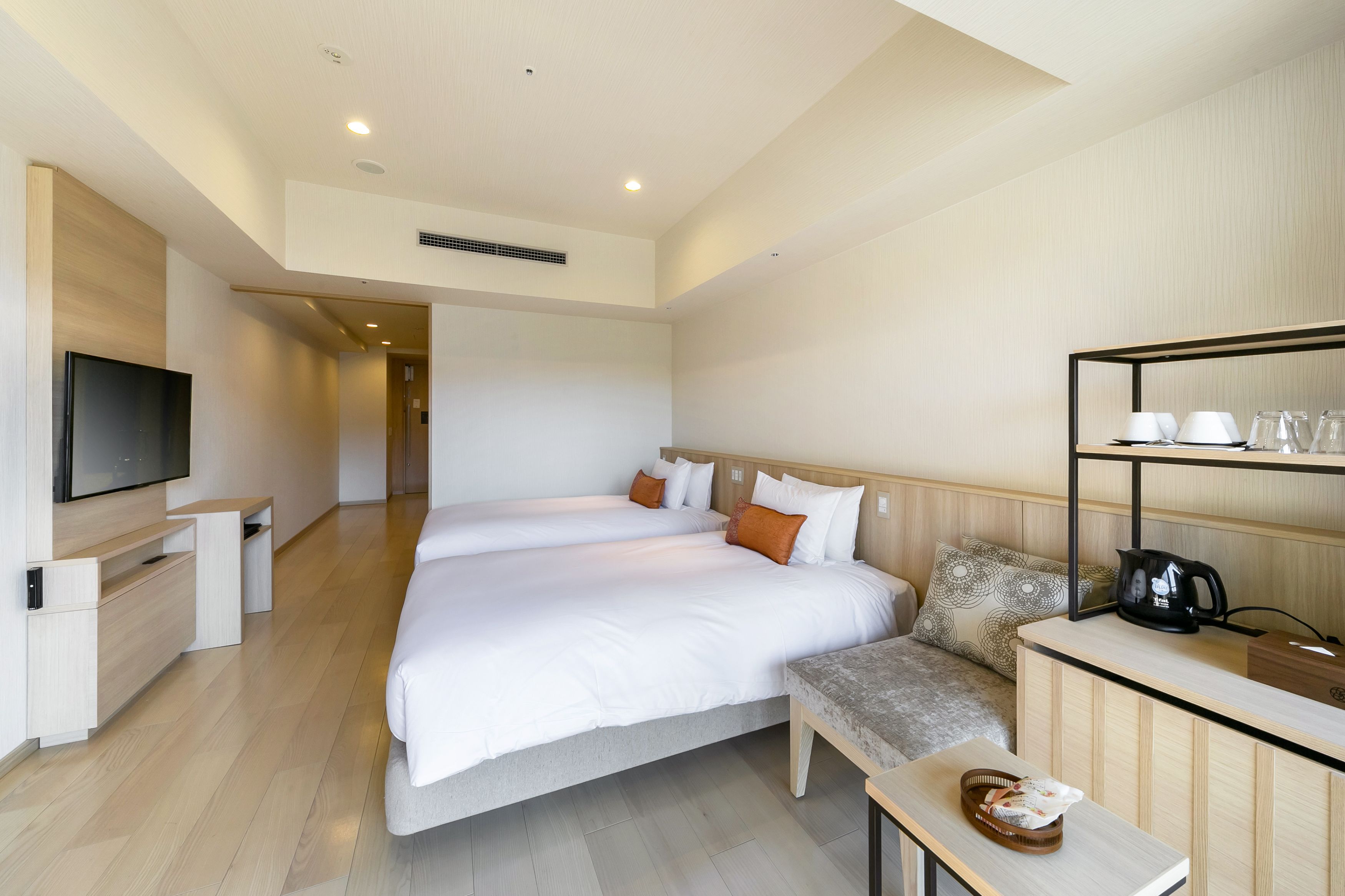 A hotel room with a large bed, a TV, a coffee machine, and a shelf with cups and glasses.