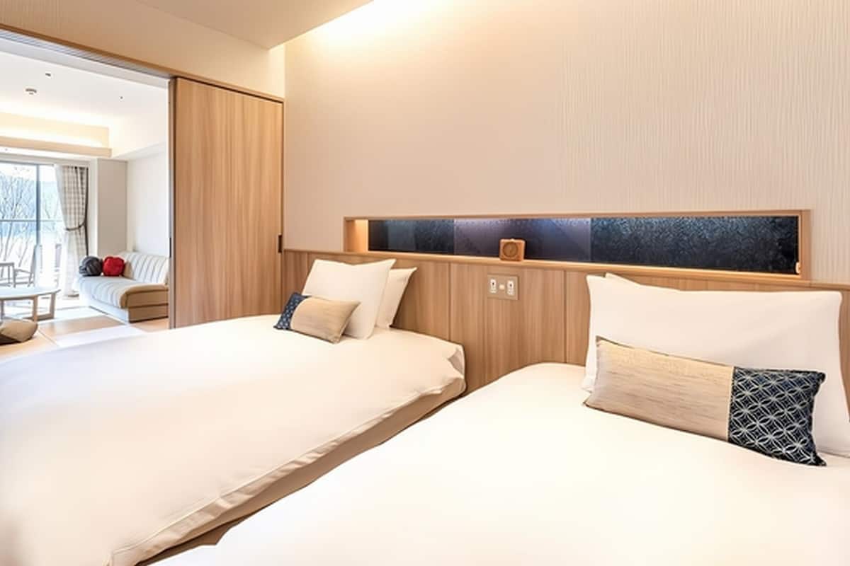 Ein modernes Hotelzimmer mit zwei Betten, einem großen Fenster, einer Couch und einem Essbereich.