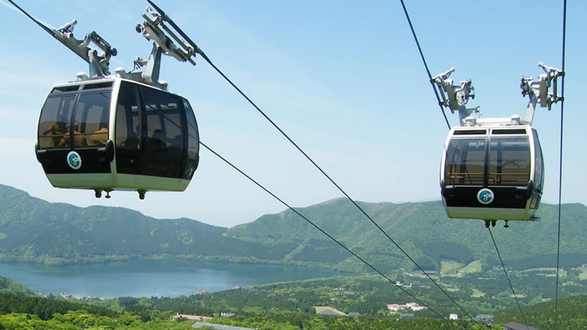 Two cable cars in motion with a mountainous landscape and a body of water in the background.