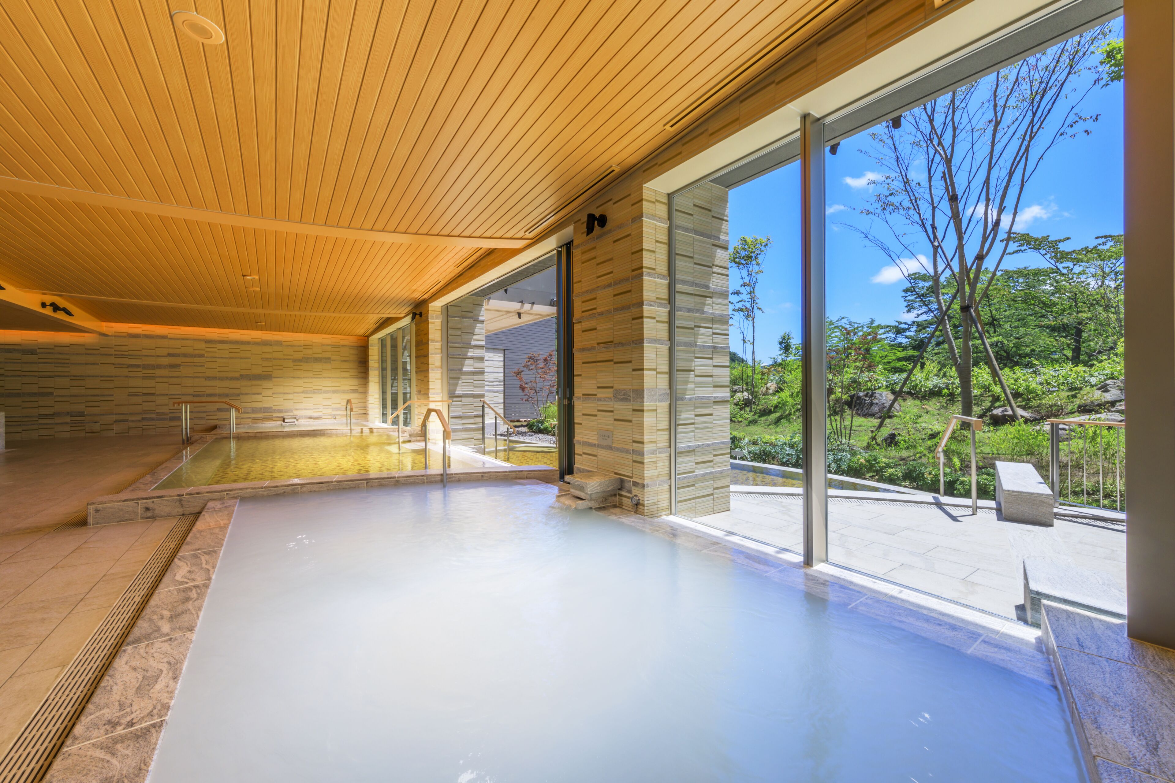 A modern indoor swimming pool with a wooden ceiling and large glass doors leading to a garden.