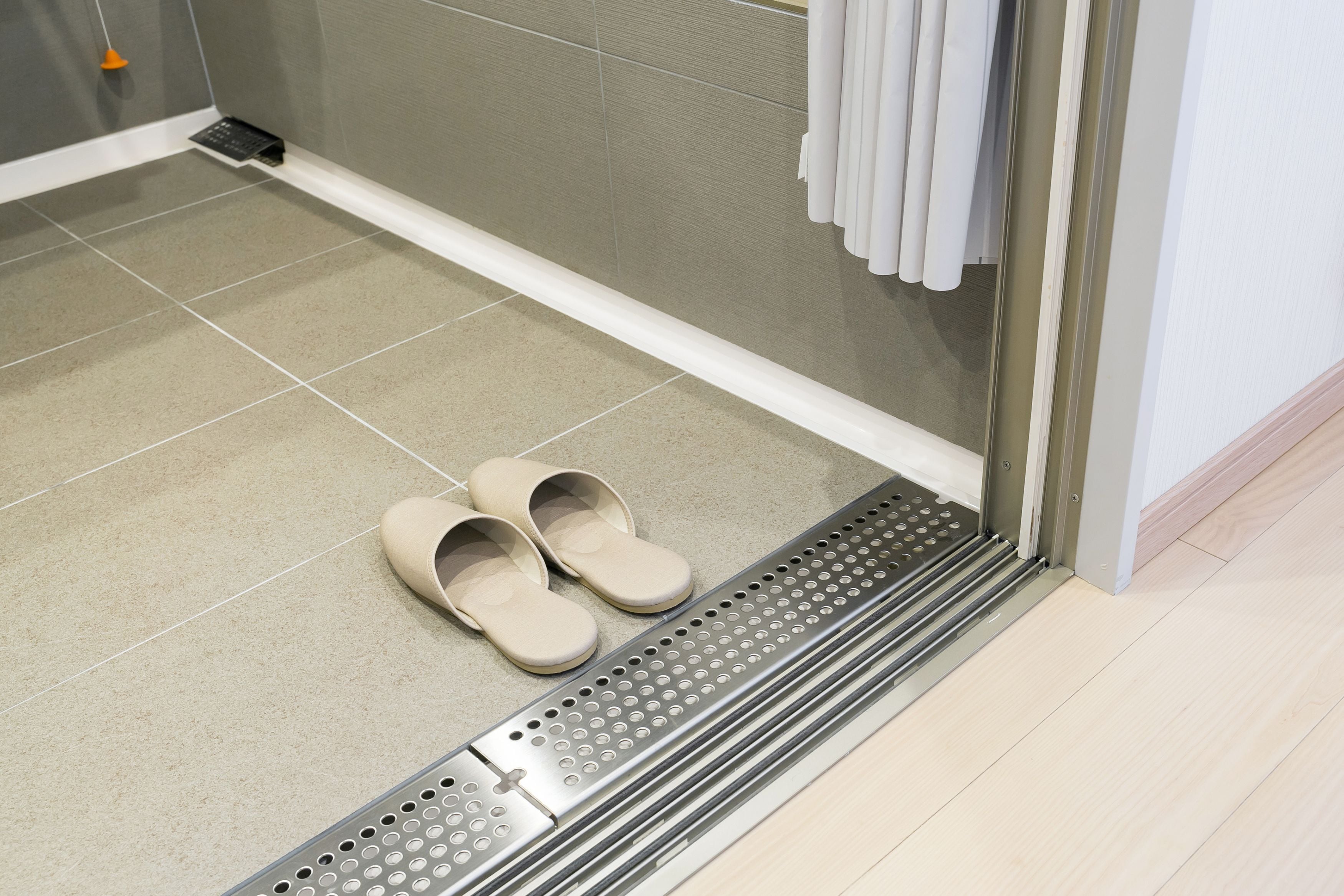 A bathroom with a shower area, a pair of slippers, and a tiled floor.