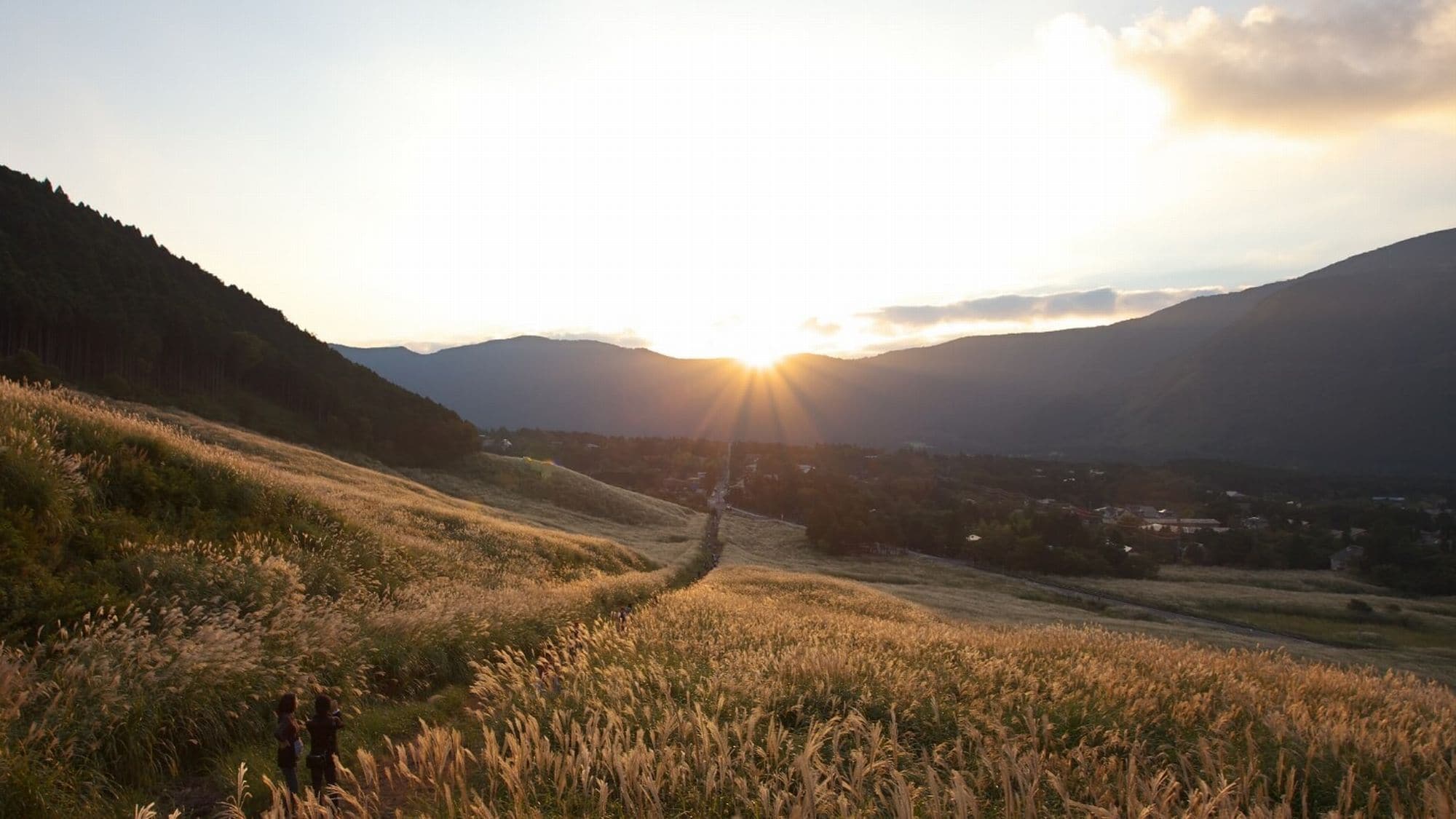 A rural landscape with rolling hills, a clear path, and a distant village.