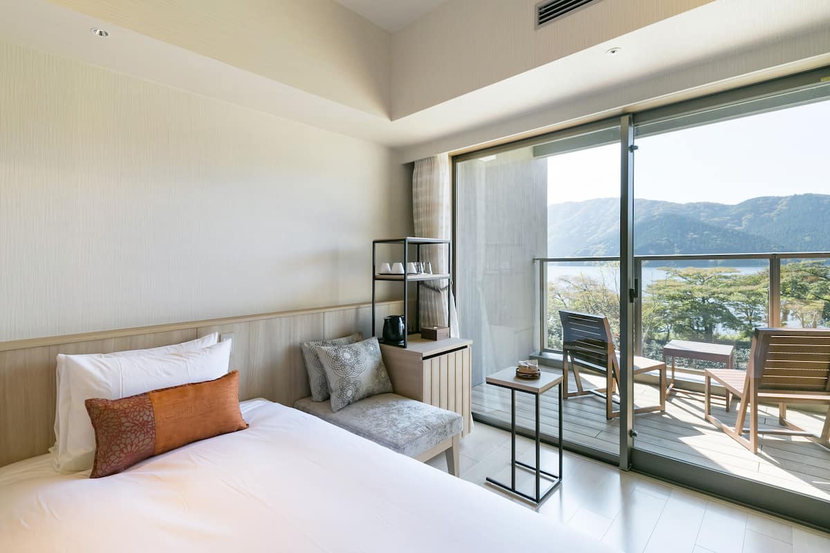 Ein modernes Hotelzimmer mit einem großen Bett, einer kleinen Sitzecke, einem Tisch und einem Balkon mit Bergblick.