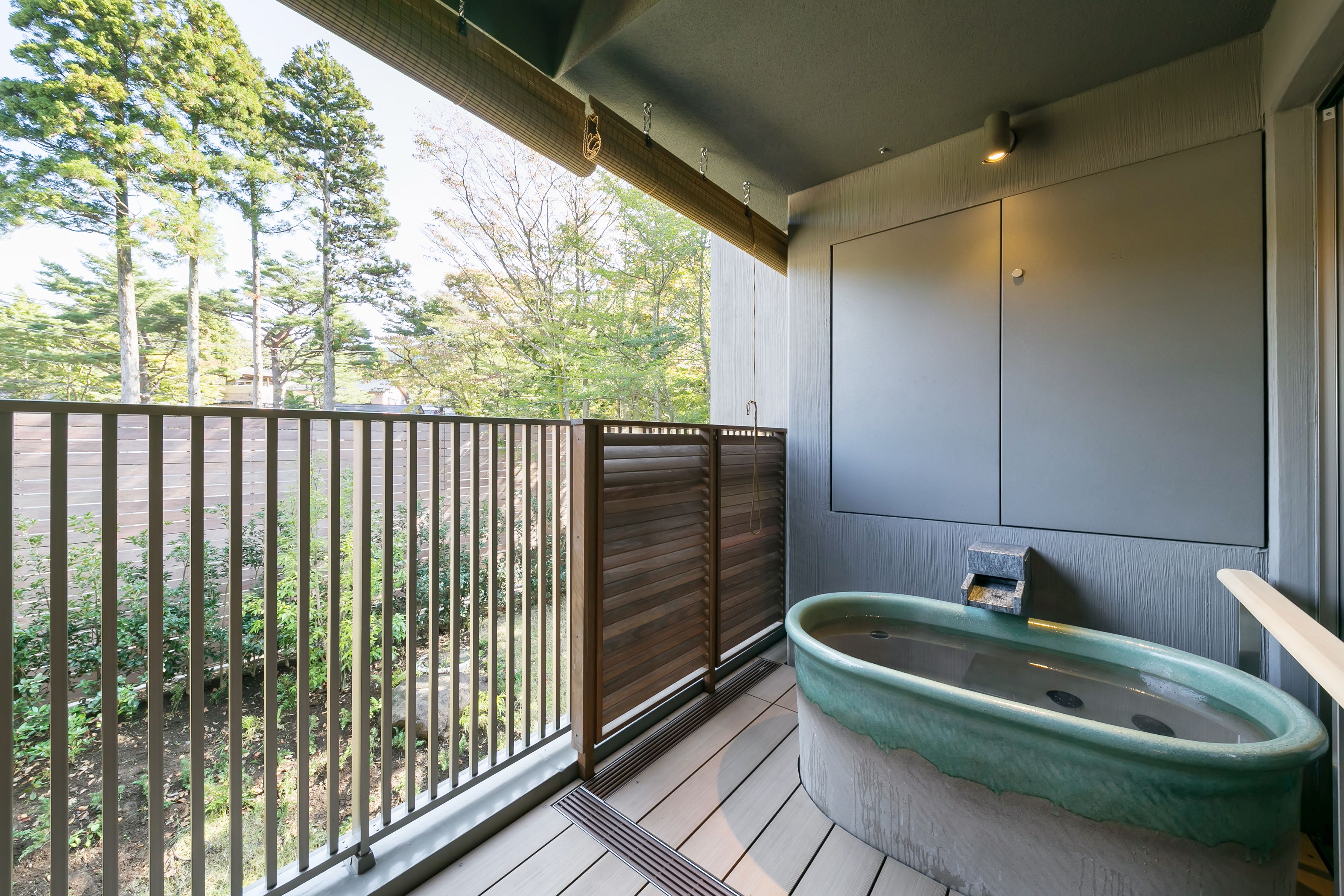 Un balcón con barandilla de madera, una bañera verde y vistas a los árboles.