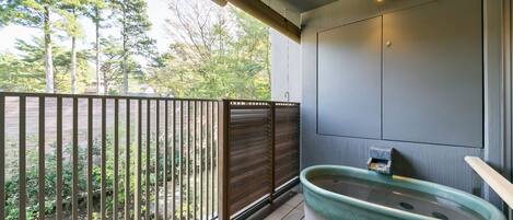 A balcony with a wooden railing, a green bathtub, and a view of trees.