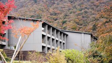 A modern building with multiple balconies, surrounded by lush greenery and a mountainous backdrop.