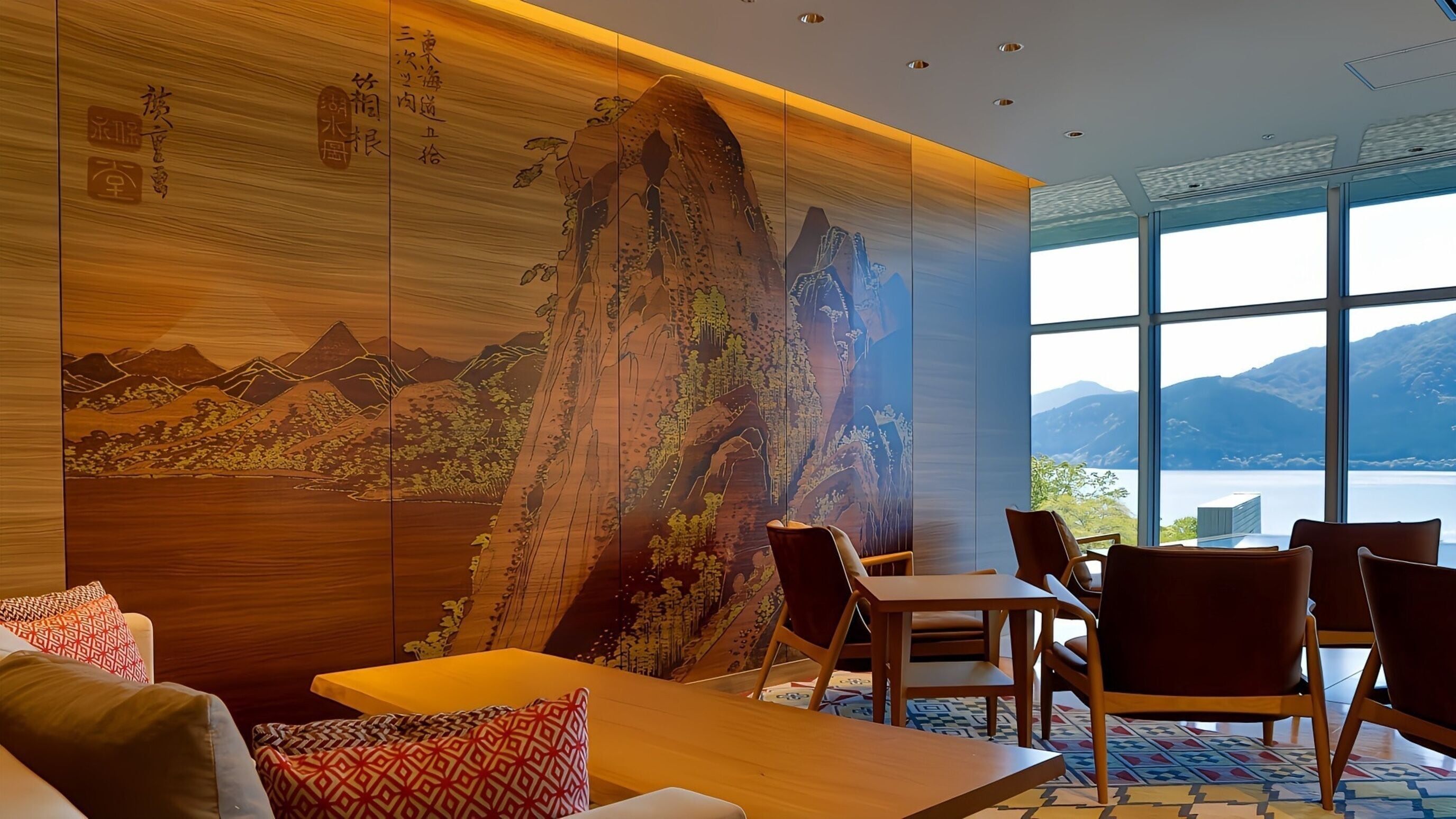 A room with a large wooden wall mural, a dining area with chairs and a table, and a view of mountains through large windows.