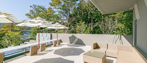 A modern outdoor patio with wicker furniture, umbrellas, and a view of the sea.