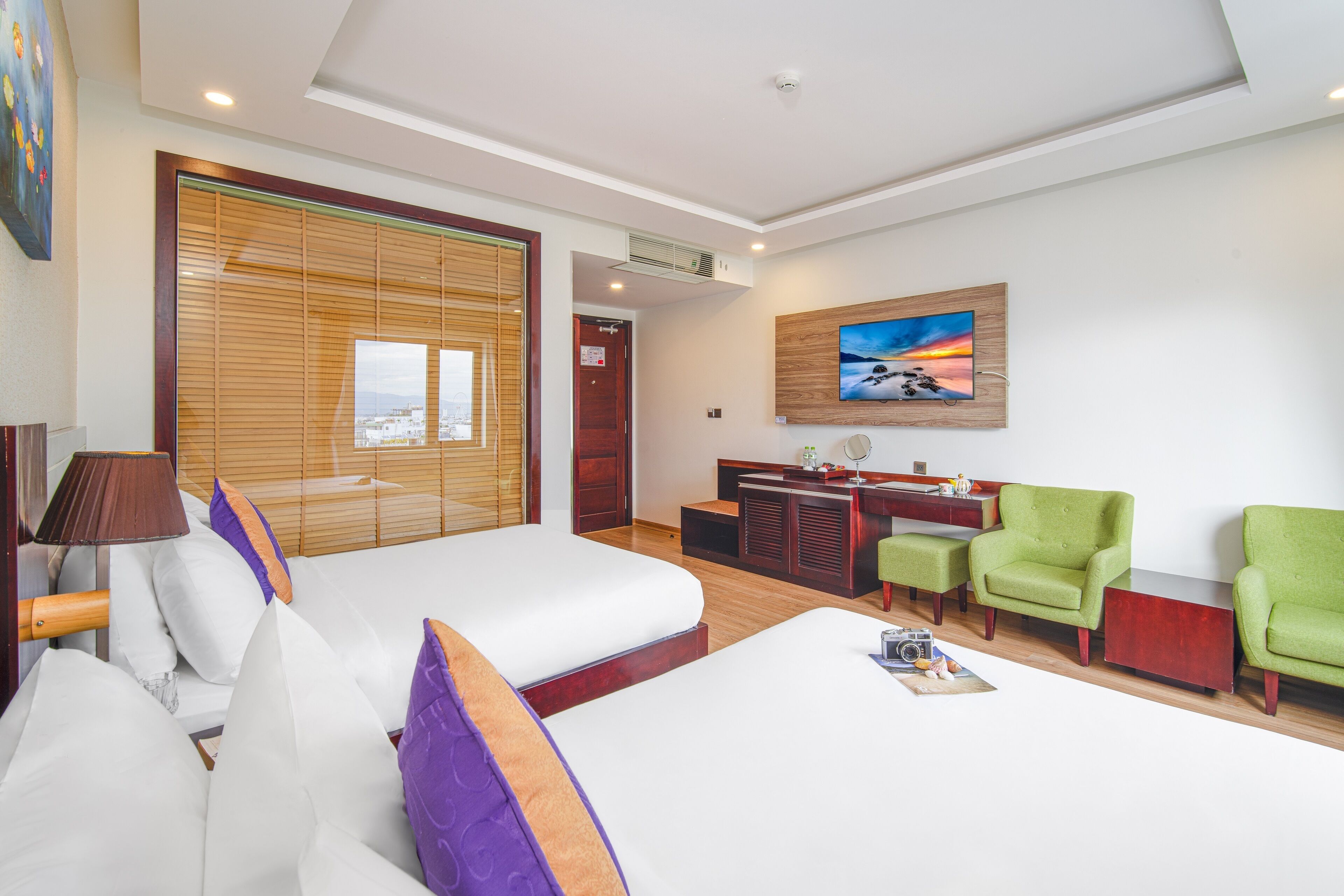 Ein Hotelzimmer mit einem Bett, einem Schreibtisch, zwei grünen Sesseln und einem Bild an der Wand.
