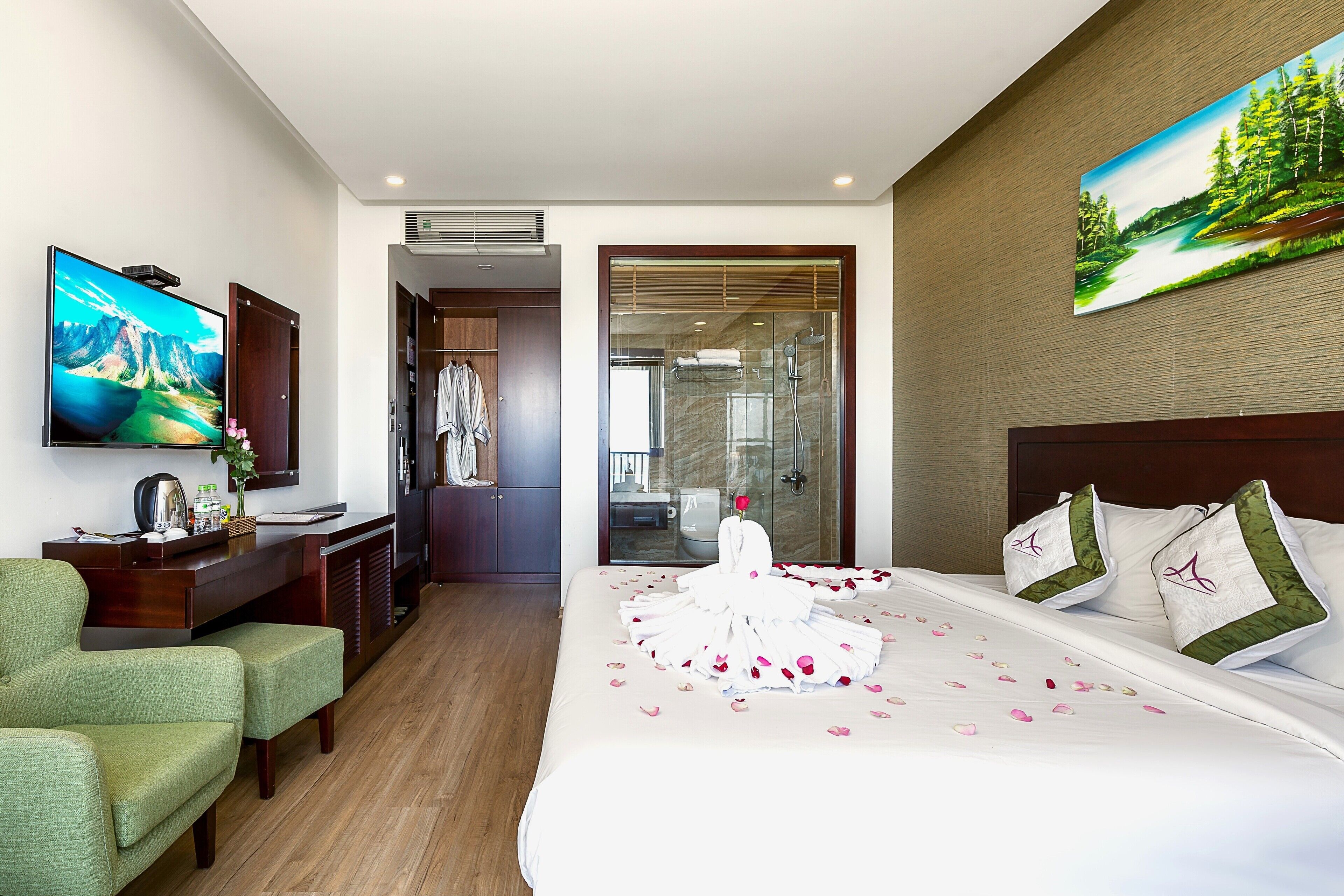 A hotel room with a bed, a desk, a television, and a painting on the wall.