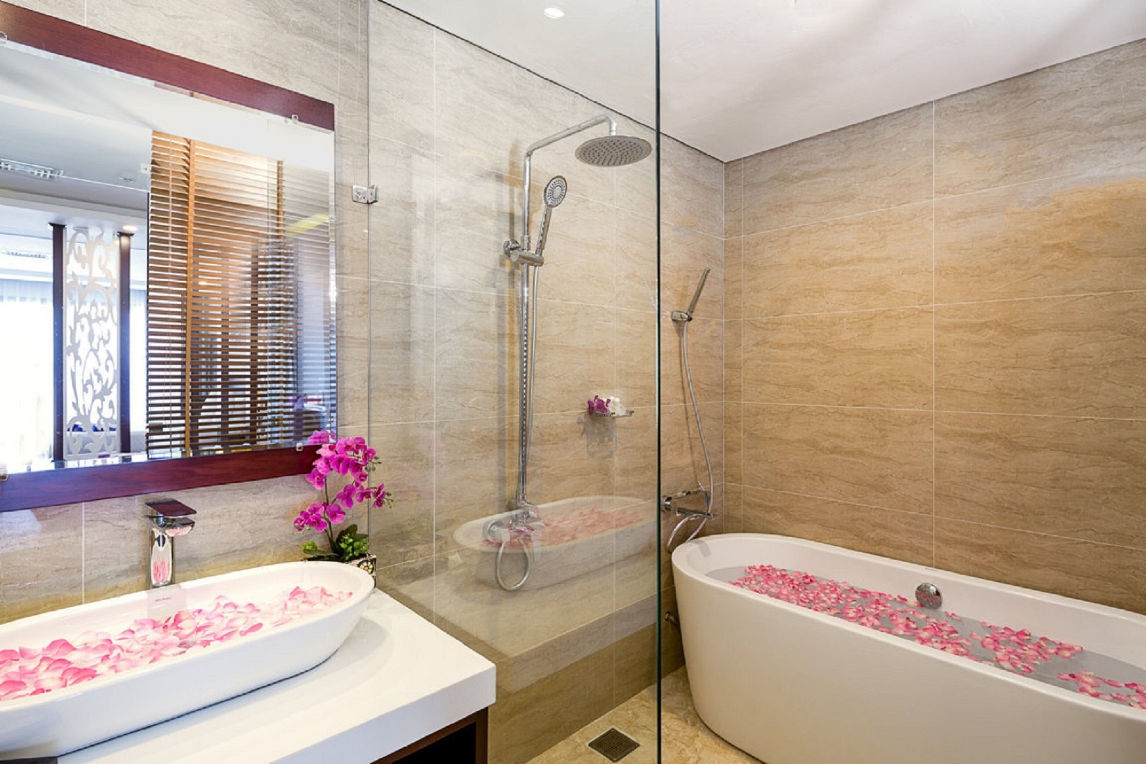 A modern bathroom with a glass-enclosed shower, a freestanding bathtub, and two sinks with rose petals.