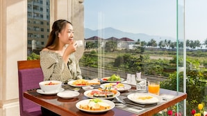 Una mesa de comedor con varios platos y un vaso de jugo de naranja, frente a una vista panorámica de montañas y palmeras.