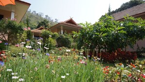 Un bâtiment traditionnel avec un toit en tuiles et un jardin où poussent différentes sortes de fleurs et de plantes.