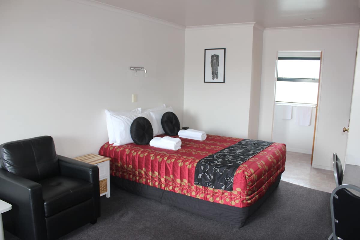 A hotel room with a bed, a black leather chair, a small table, and a door.