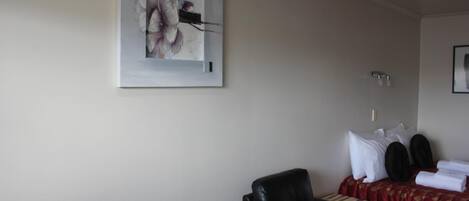 Habitación de hotel con cama, sillón de masajes, una obra de arte en la pared y una mesita con una revista.