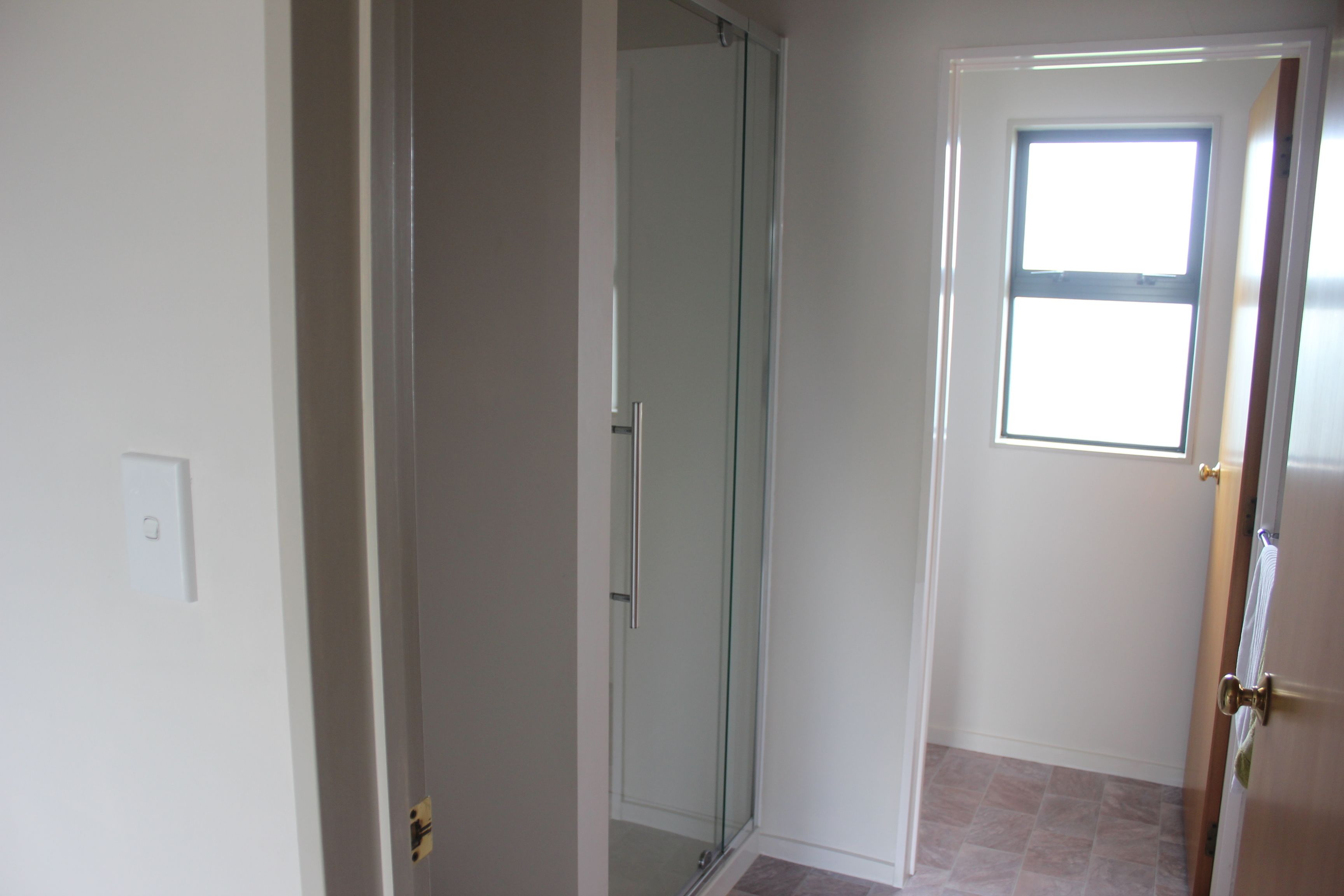 A room with a glass shower door, a door with a window, and a light switch on the wall.