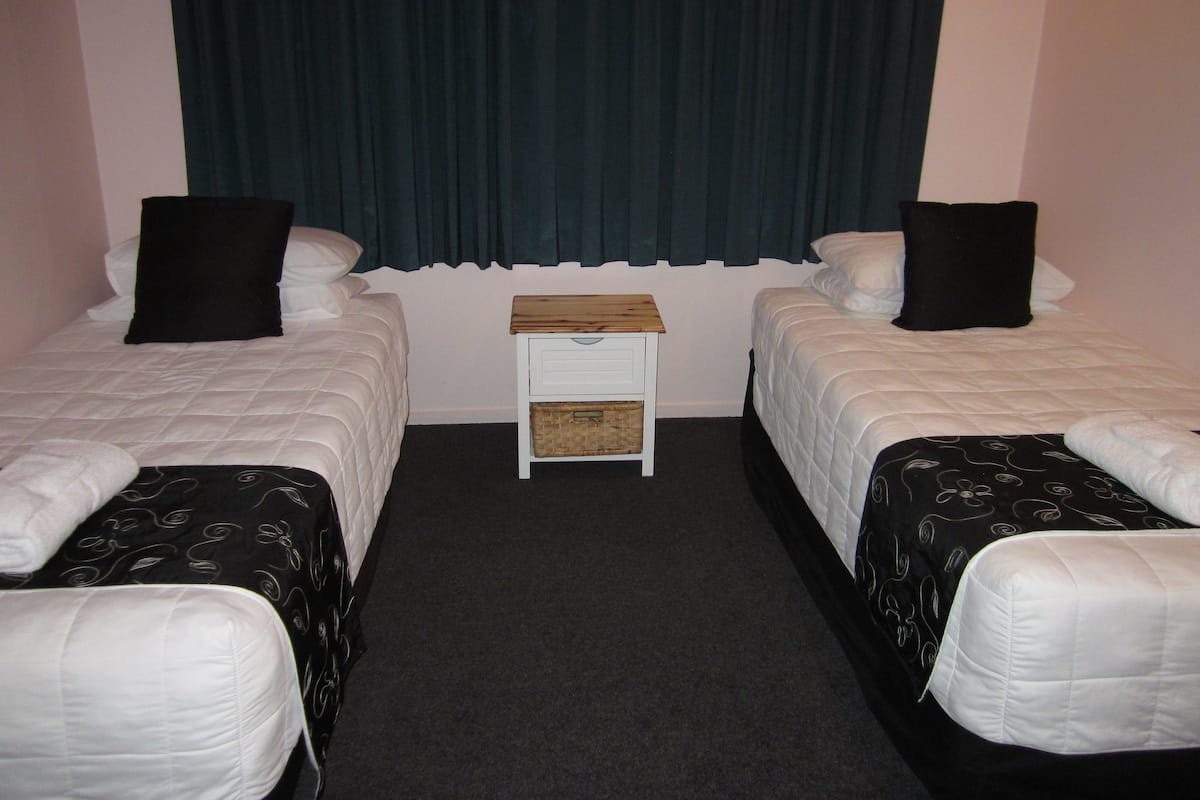 A hotel room with two single beds, a small wooden nightstand, and a dark curtain.