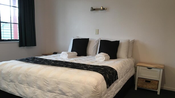 A neatly made bed with white and black bedding, a bedside table with a basket, and a window with curtains.