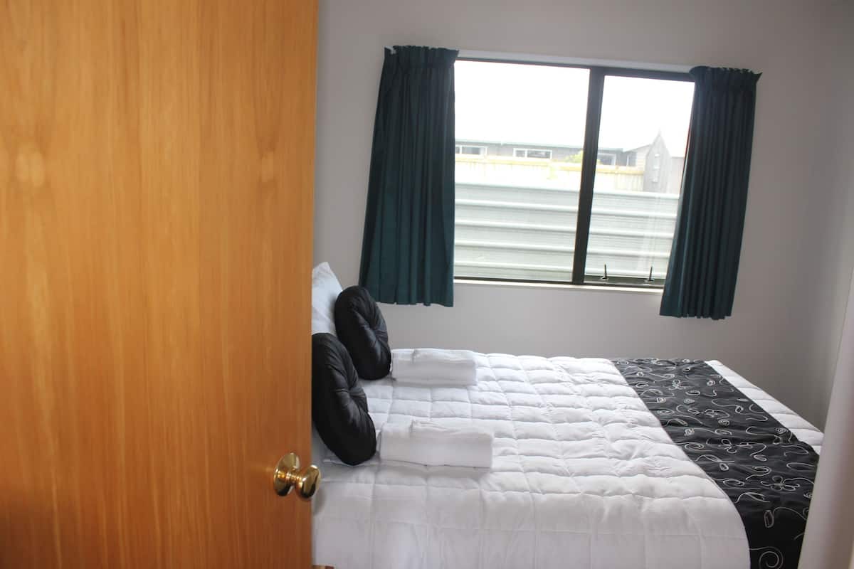 A hotel room with a bed, a window with curtains, and a view of a building outside.