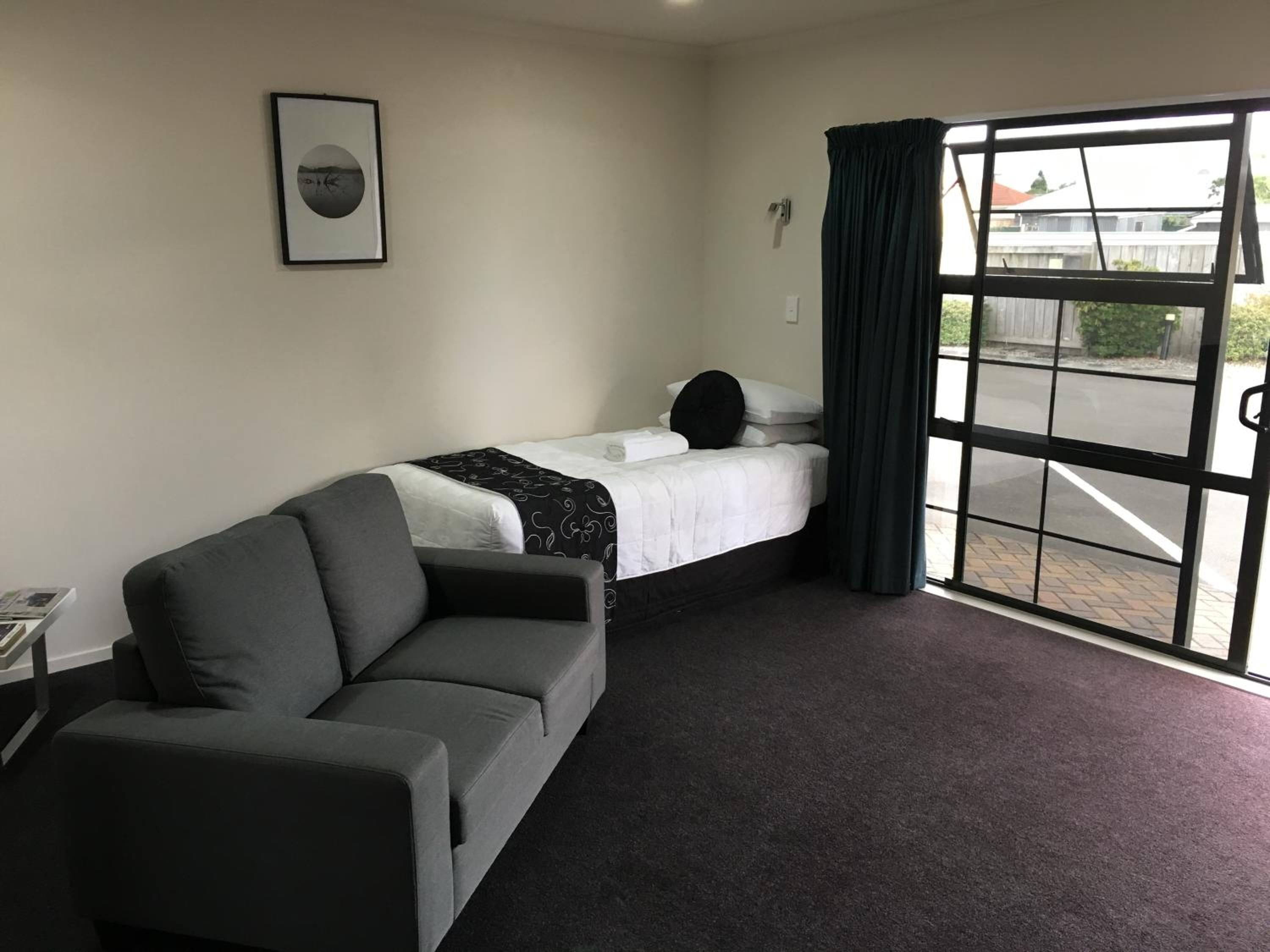 Una habitación con una cama, un sofá, un cuadro en la pared y una ventana con cortinas.