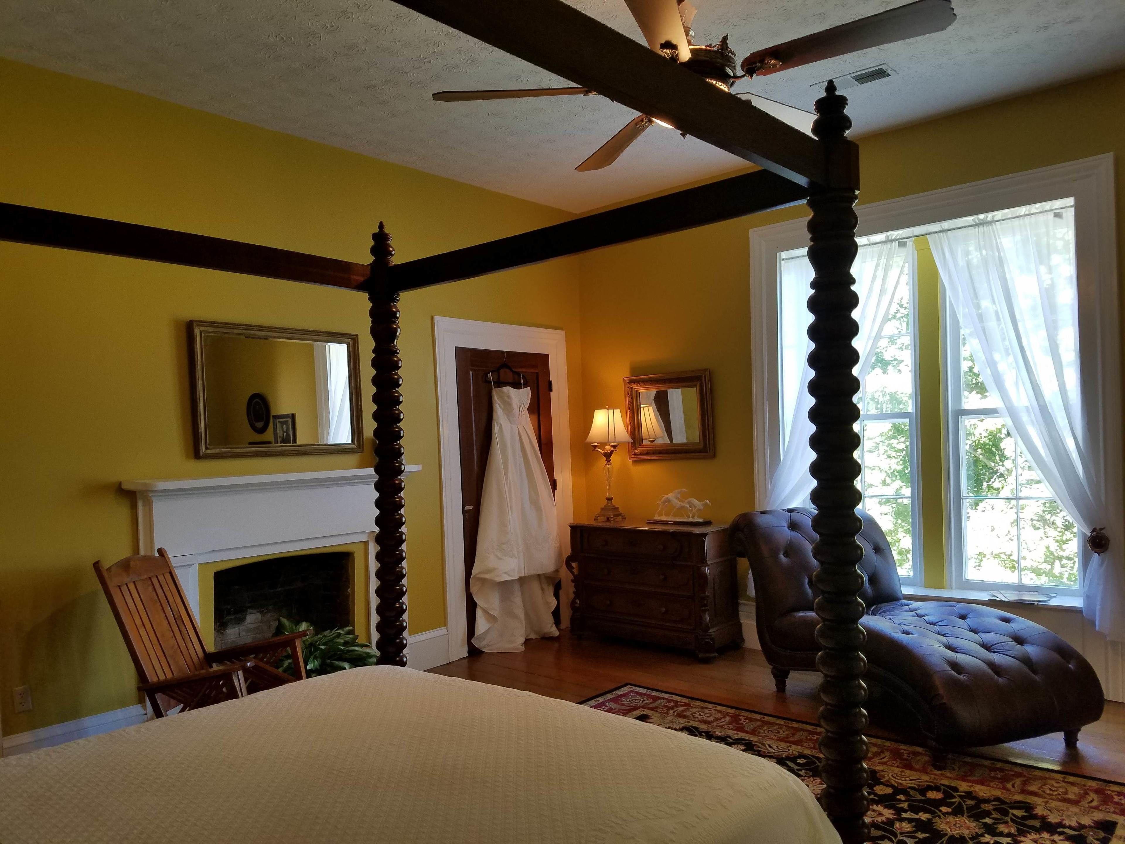 Quarto com cama de dossel, lareira, janela grande com cortinas e ventoinha de teto.