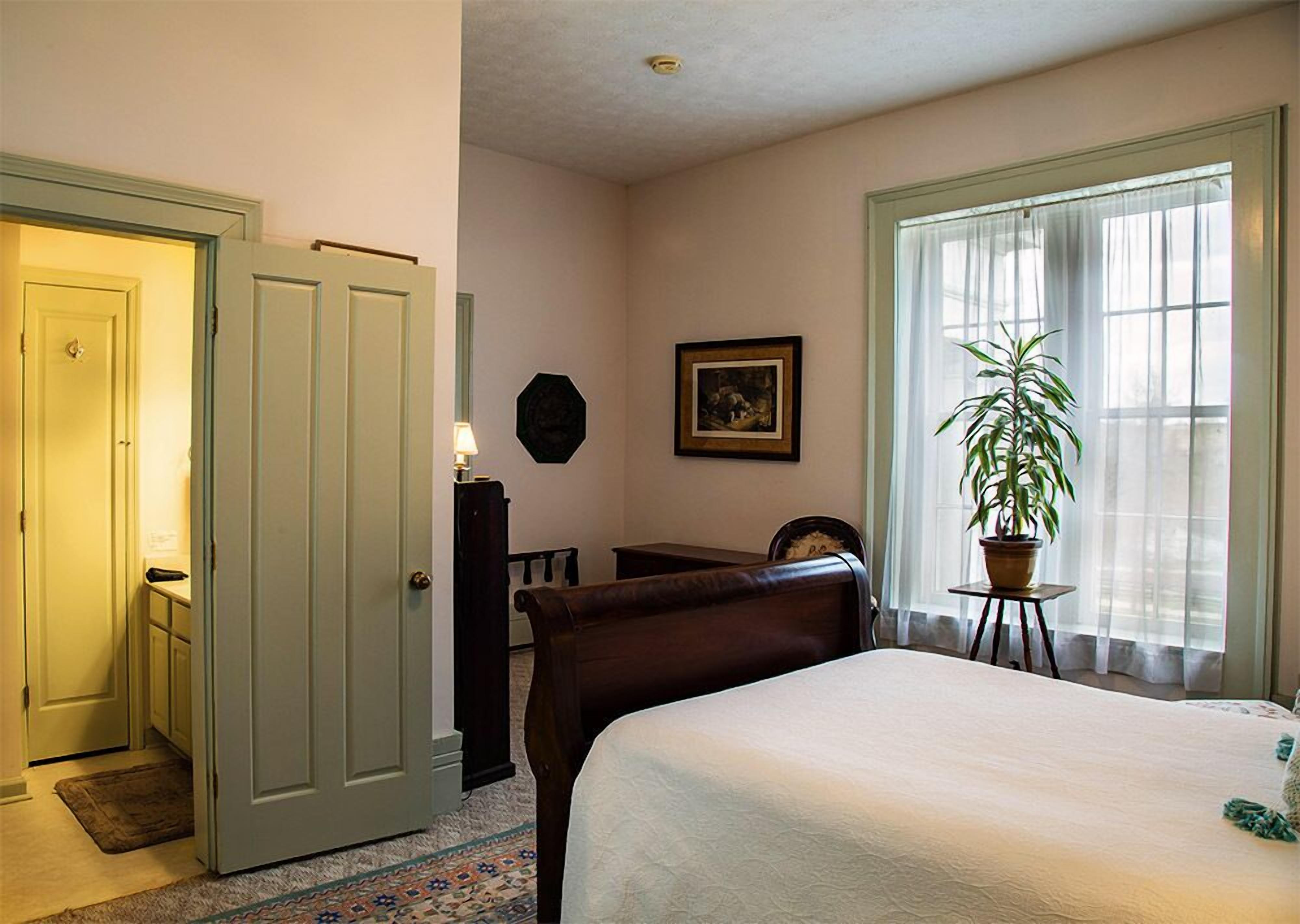 A bedroom with a bed, a desk, a chair, a potted plant, and a window with curtains.