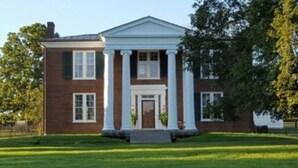 A two-story brick building with a central entrance flanked by columns, a front lawn, and trees. - The Denny House (Paint Lick)