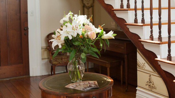 A staircase with wooden balusters and a vase with flowers on a table. - The Denny House (Paint Lick)