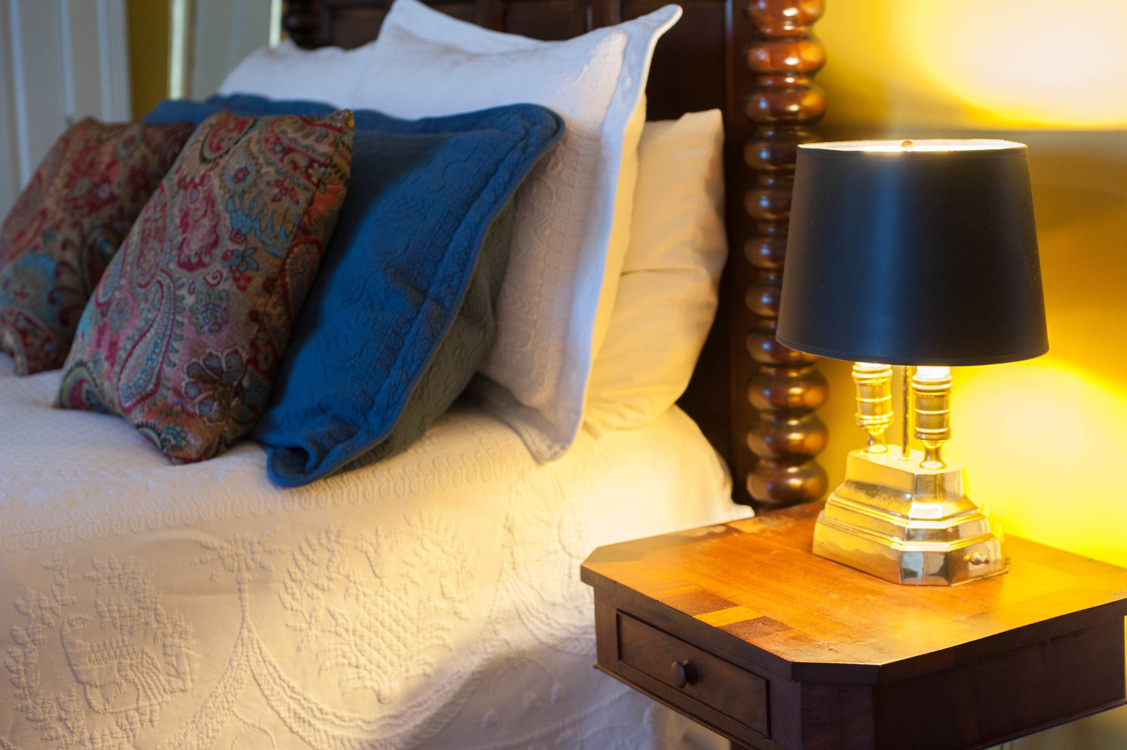 A neatly made bed with patterned pillows, a bedside lamp, and a wooden nightstand.