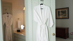 A bathroom with a white robe hanging on a door, a towel rack, and a mirror. - The Denny House (Paint Lick)