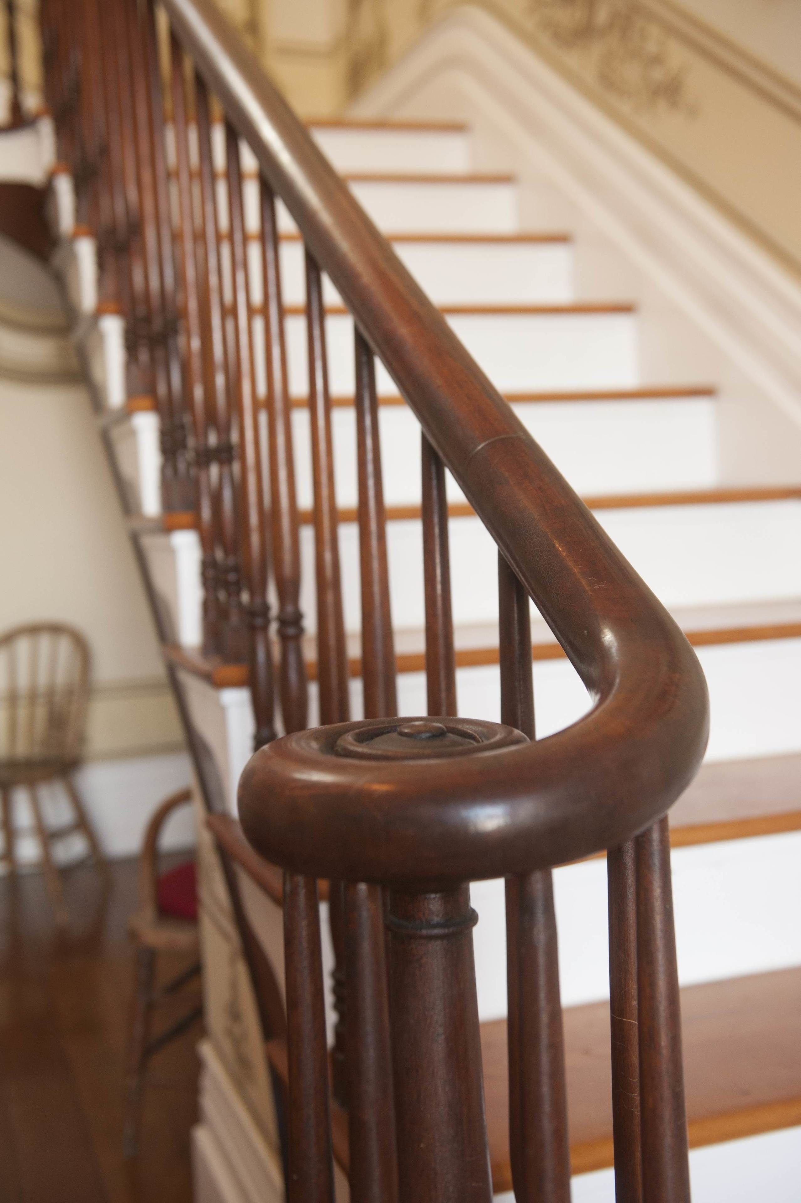 A wooden staircase with a handrail and a white wall with a decorative molding in the background.