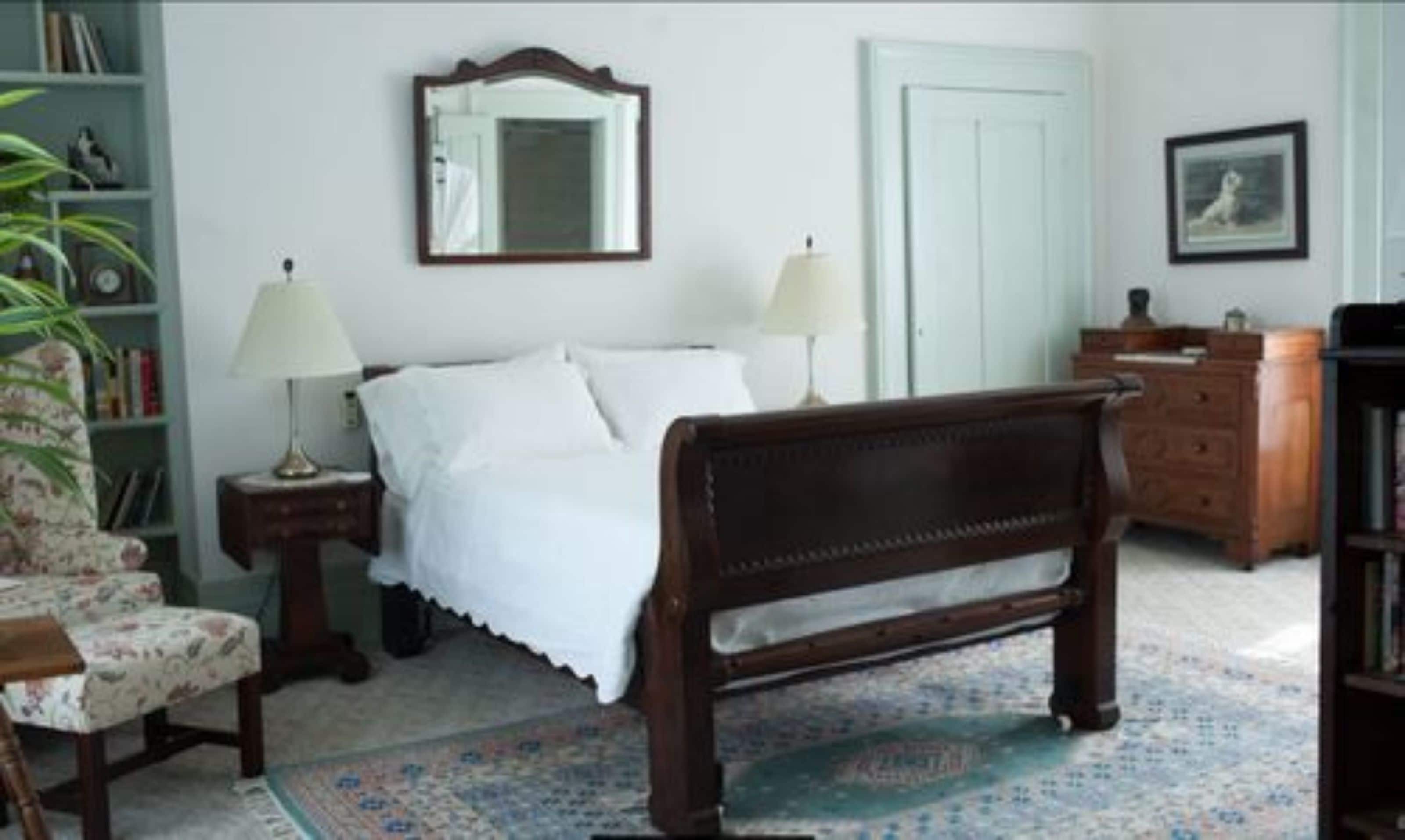 Un dormitorio con una cama de madera, dos mesitas de noche con lámparas, una silla, una estantería y una puerta.