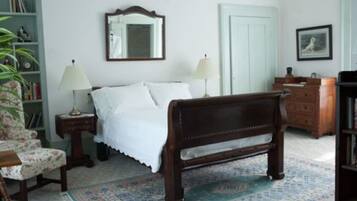 Un dormitorio con una cama de madera, dos mesitas de noche con lámparas, una silla, una estantería y una puerta.