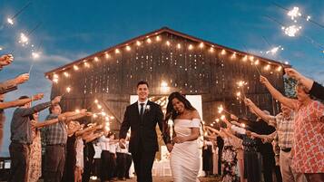 A wedding ceremony with guests holding sparklers in front of a barn-like structure.