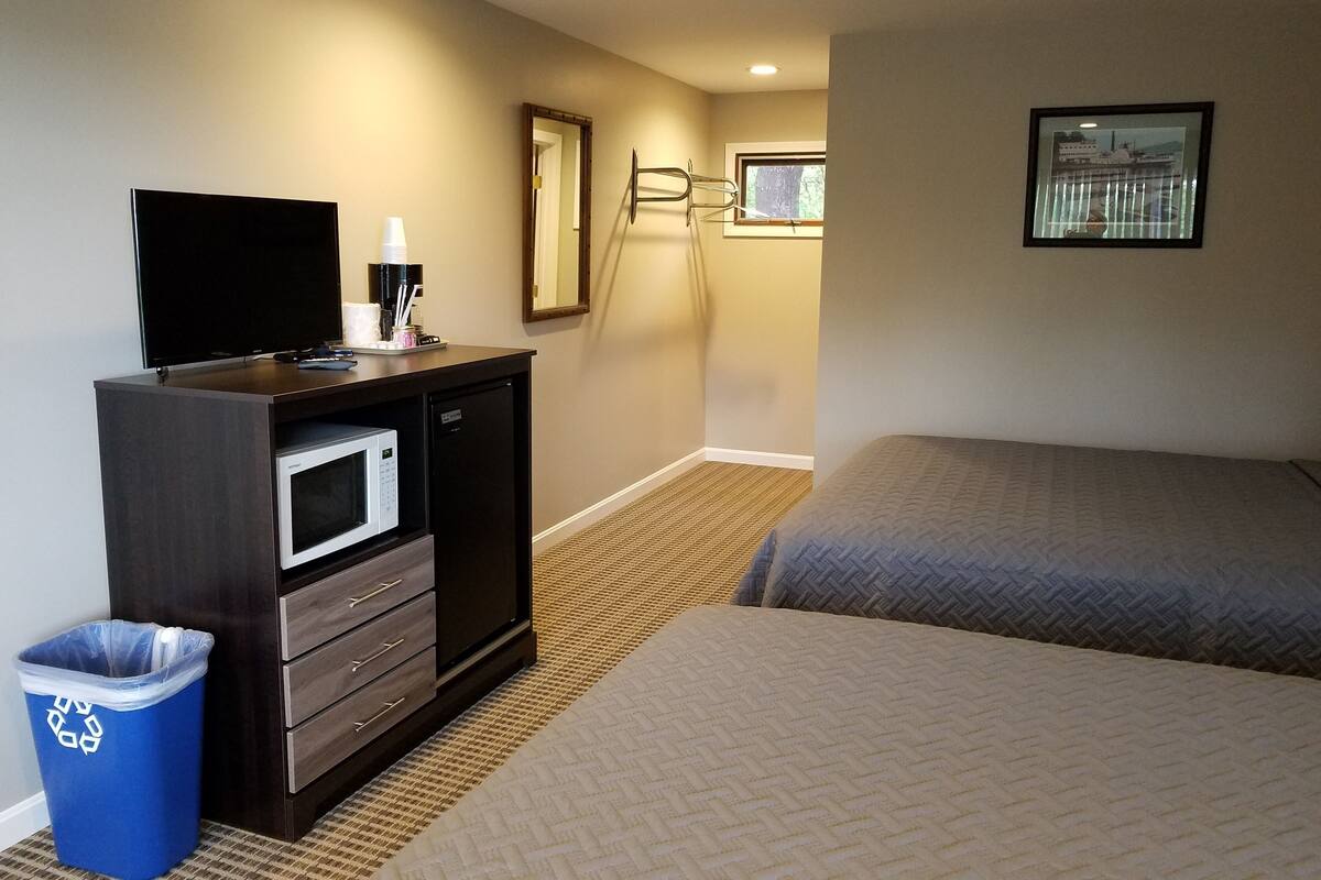 A hotel room with a bed, a TV, a microwave, a trash bin, and a window with a view of a building.
