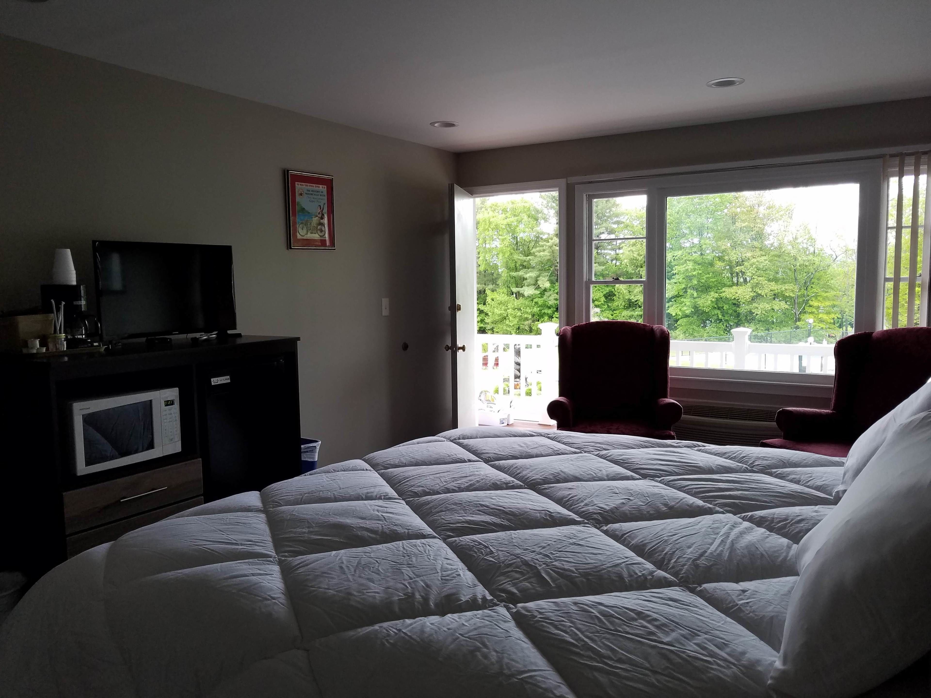 A bedroom with a large bed, a television on a dresser, and a view of greenery outside.