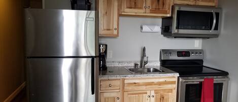 Una cocina compacta con electrodomésticos de acero inoxidable, gabinetes de madera, un microondas y un horno Bosch.