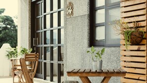Una terraza de madera con una mesa y sillas, una planta colgante y una ventana con persianas.