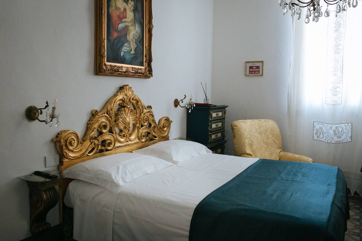 Um quarto com uma cama grande, uma cadeira, uma cômoda, um quadro na parede e um candelabro.