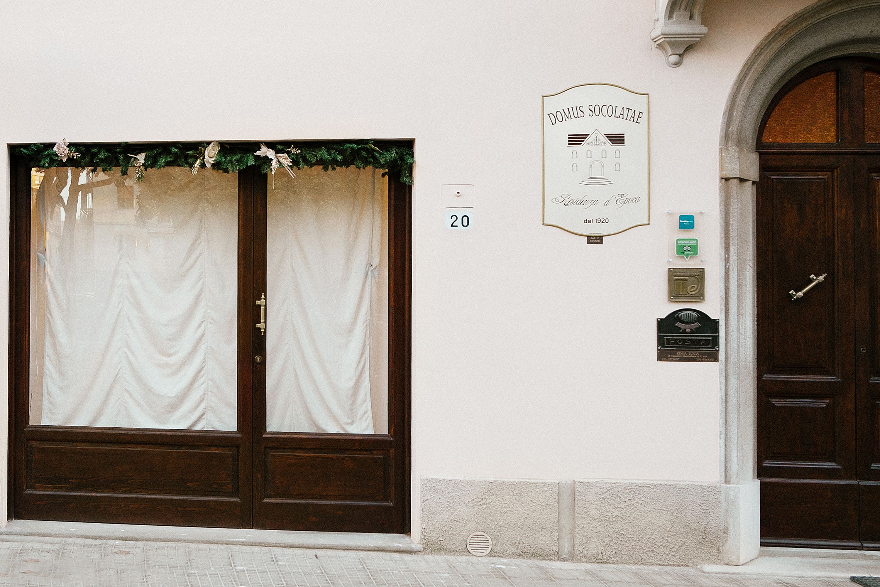 A building facade with a large wooden door, a number '20' above the door, and a sign above it.