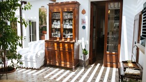 Una habitación con un sofá blanco, un aparador de madera con puertas de cristal, una planta en maceta y un suelo estampado.