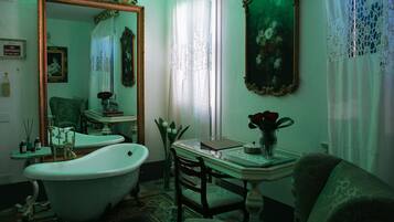 A vintage bathroom with a clawfoot bathtub, a large ornate mirror, and a classic vanity table.
