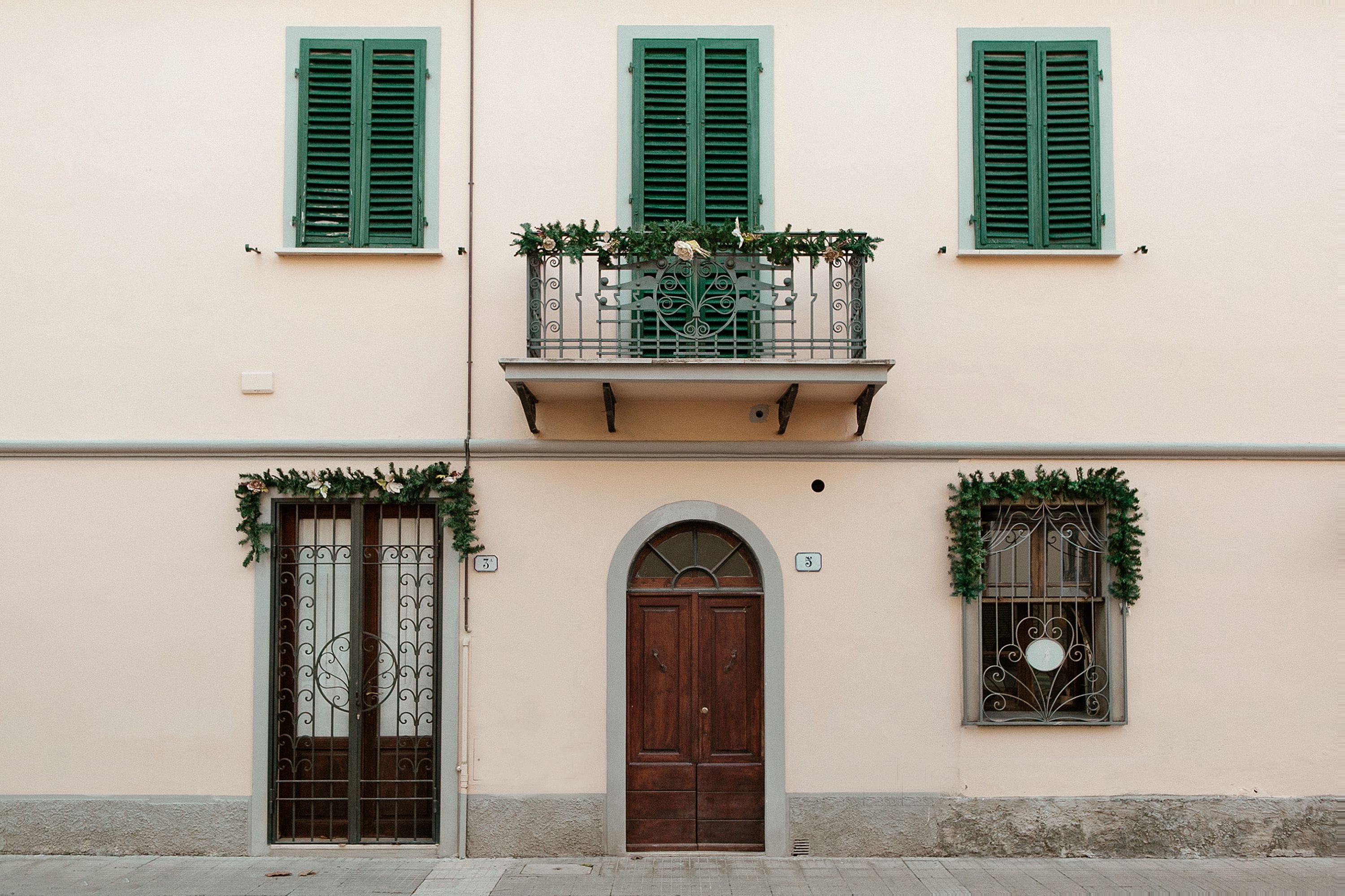 Un immeuble doté d’un balcon, d’une porte en bois et de deux fenêtres avec des volets verts.