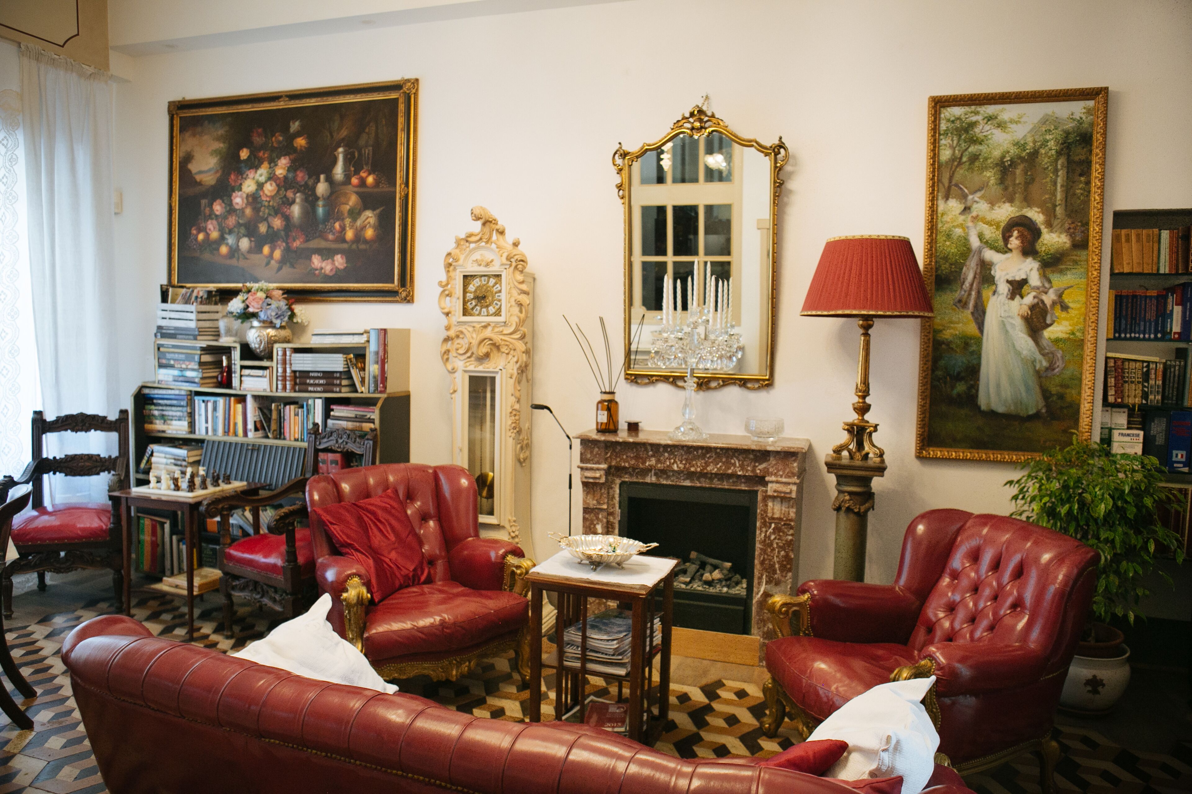 A traditional living room with leather armchairs, a fireplace, a bookshelf, and a large floral painting.