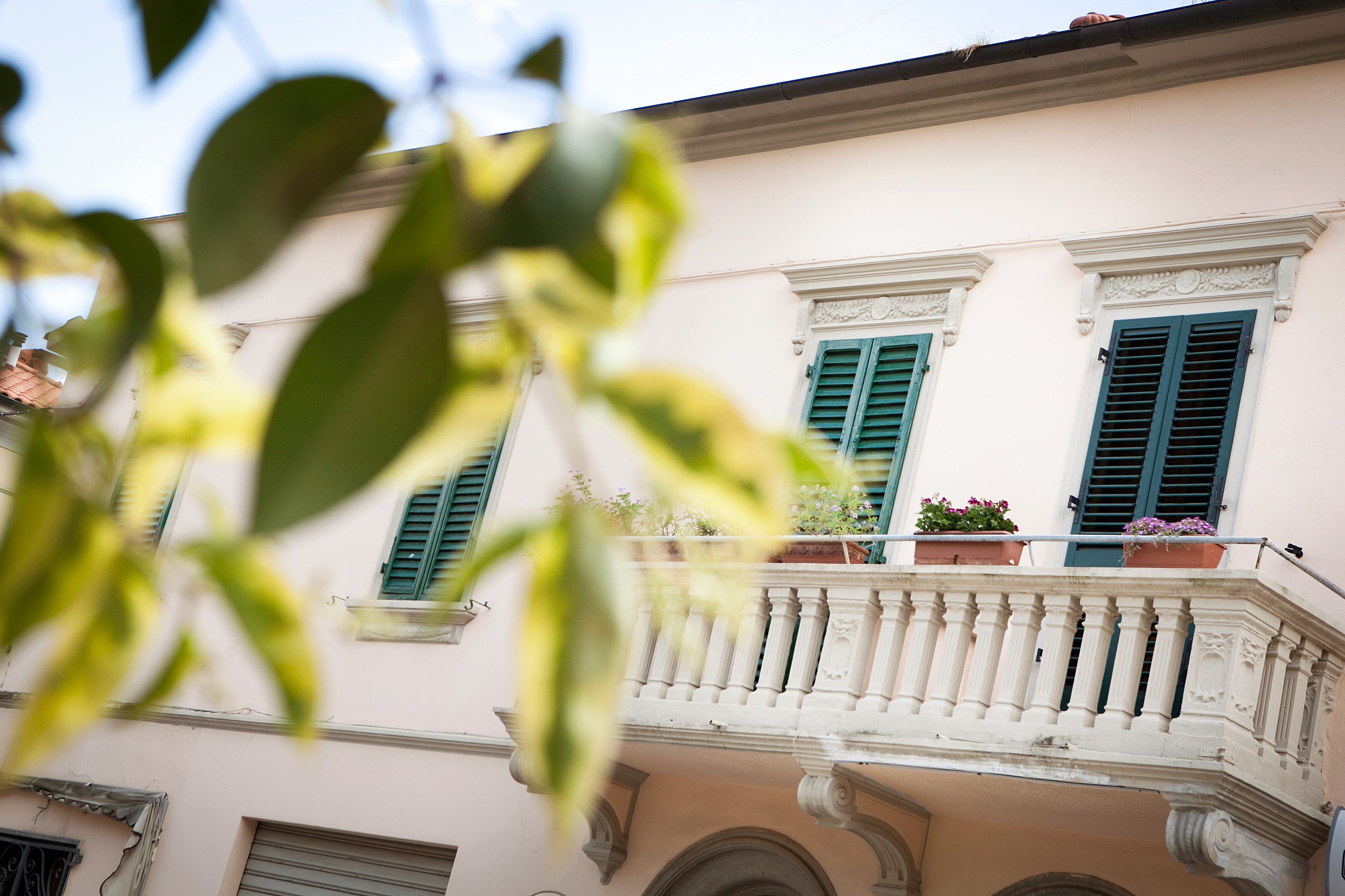 A building with a balcony, green shutters, and potted plants.