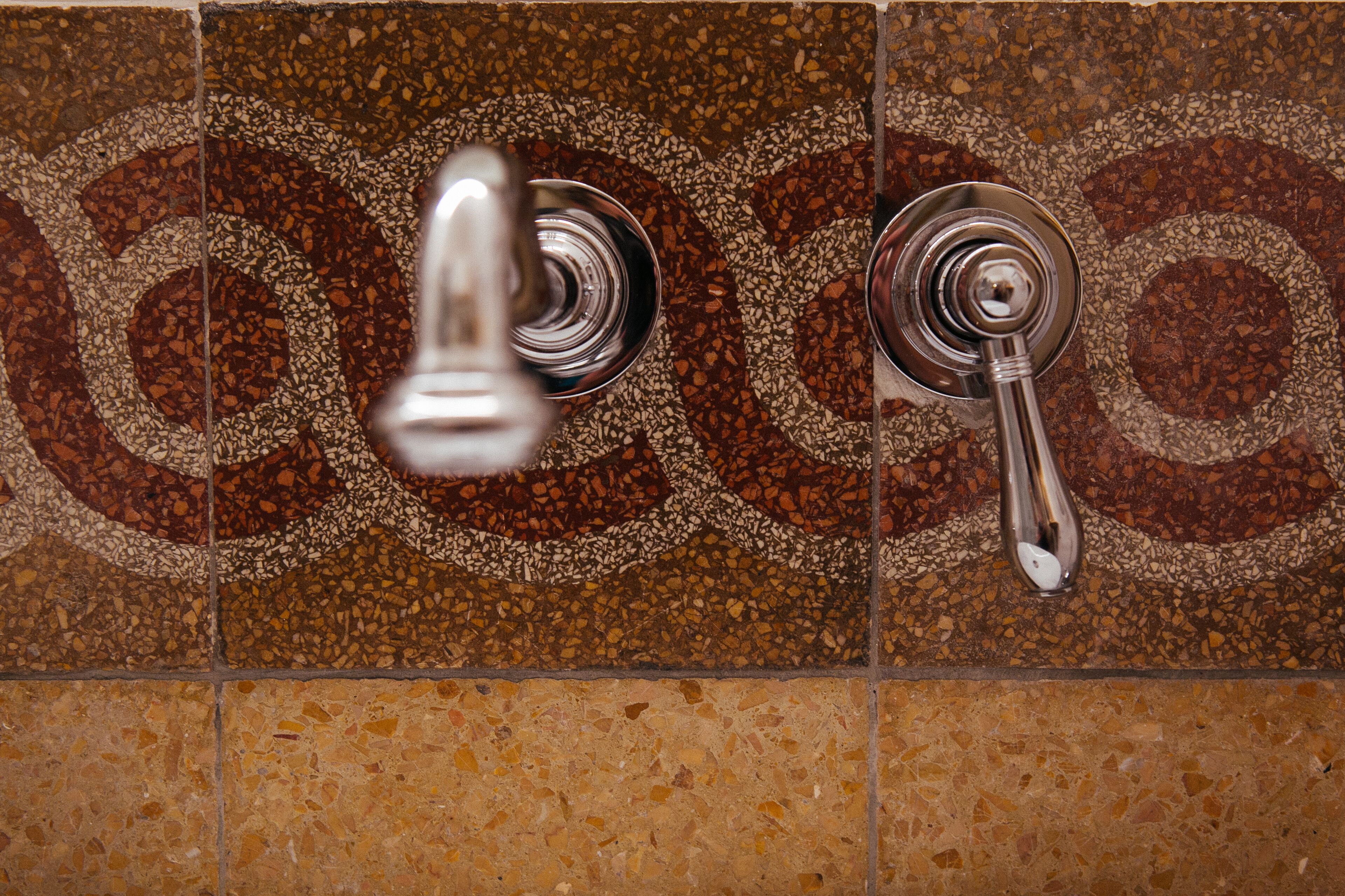 A bathroom with a tiled wall featuring a mosaic pattern and two chrome faucets.