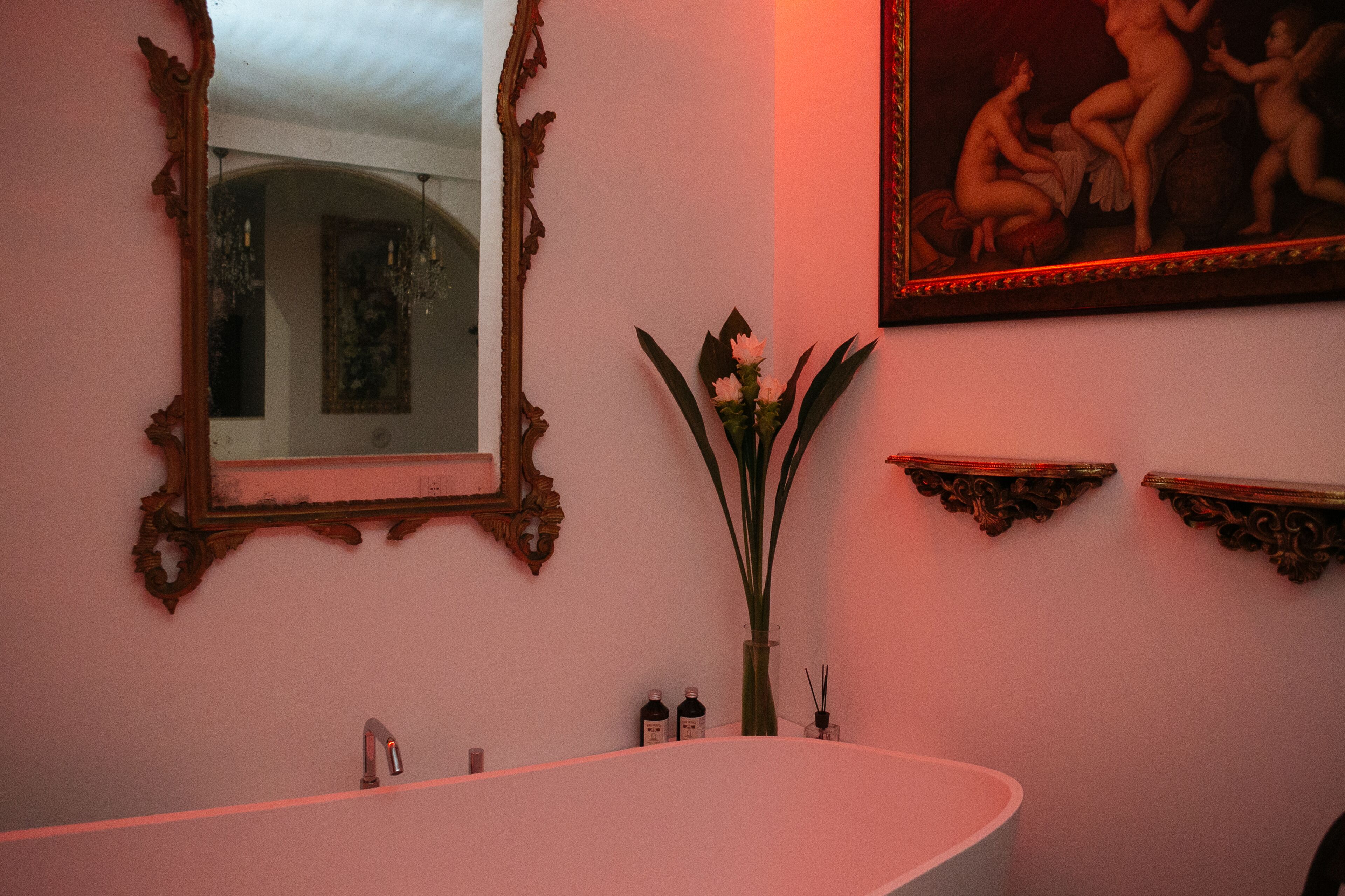 A bathroom with a freestanding bathtub, a large mirror, and a framed painting on the wall.