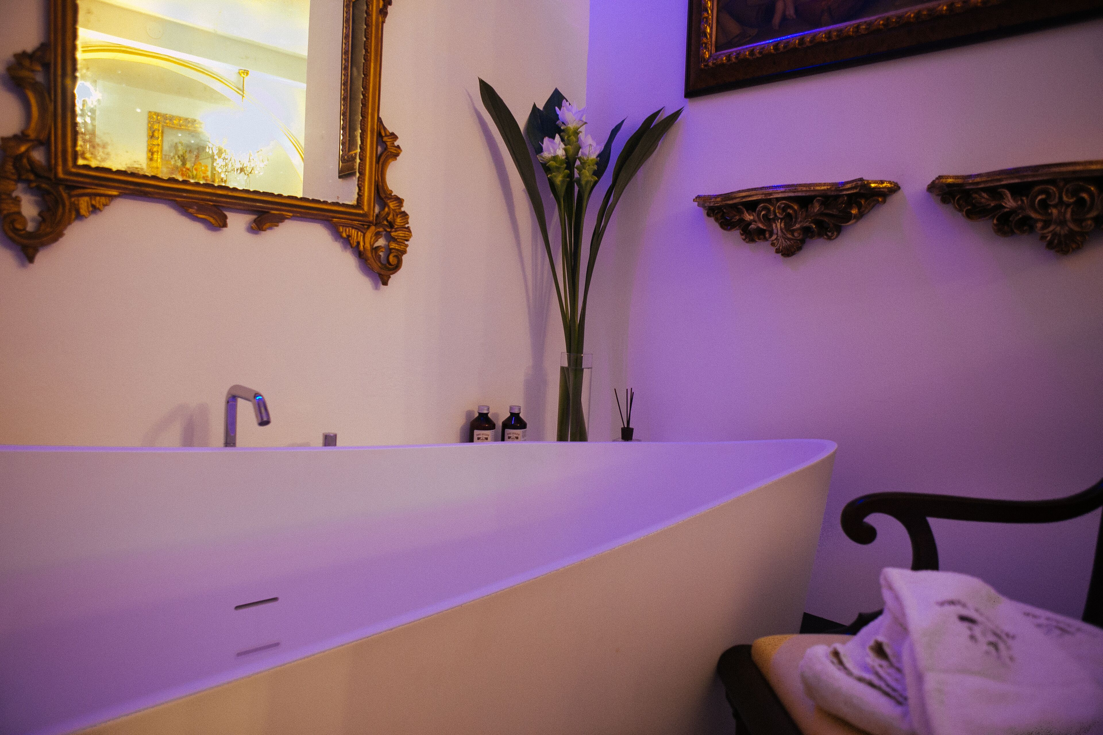 Un baño con una bañera independiente, un espejo y apliques decorativos.