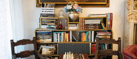 Una habitación con un tablero de ajedrez, estanterías llenas de libros, un jarrón con flores y un cuadro en la pared.