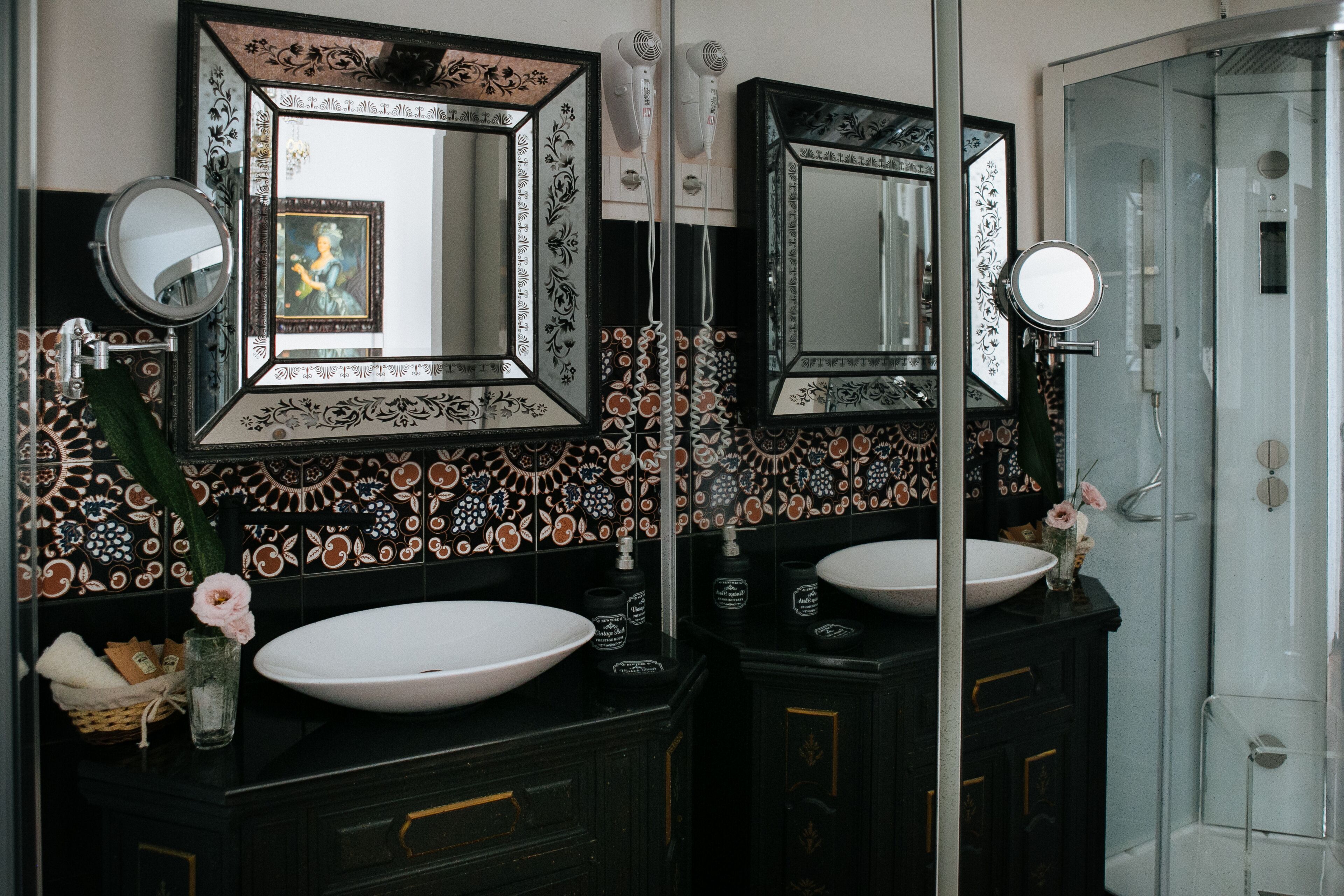 Un baño con dos lavamanos, espejos decorativos y una ducha.